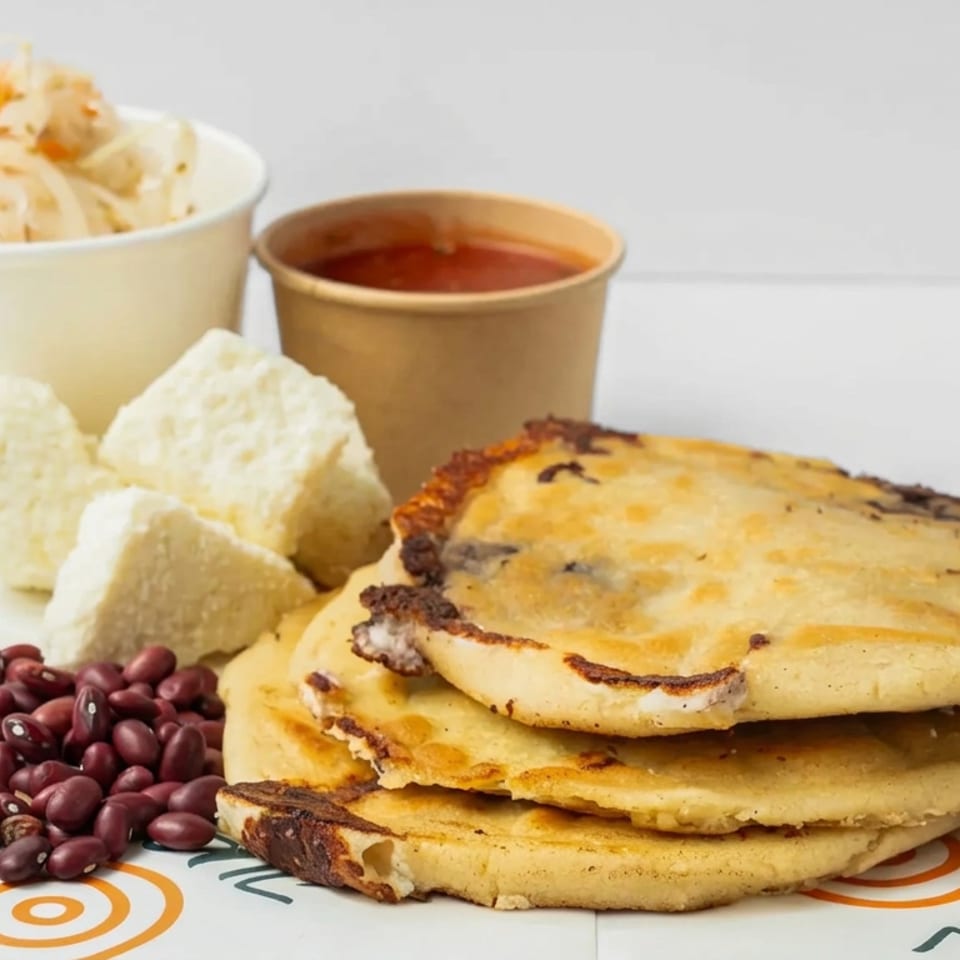 Stacked golden arepas with melted cheese, red beans, white cheese crisps, creamy slaw, and red sauce.