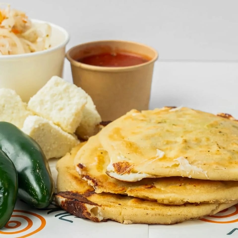 Stacked golden pupusas served with jalapeños, cabbage slaw, red salsa, and crisp tortilla chips.