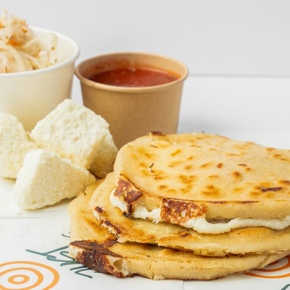 Stacked golden arepas filled with white cheese, served with shredded salad, sauce, and fried plantain slices.